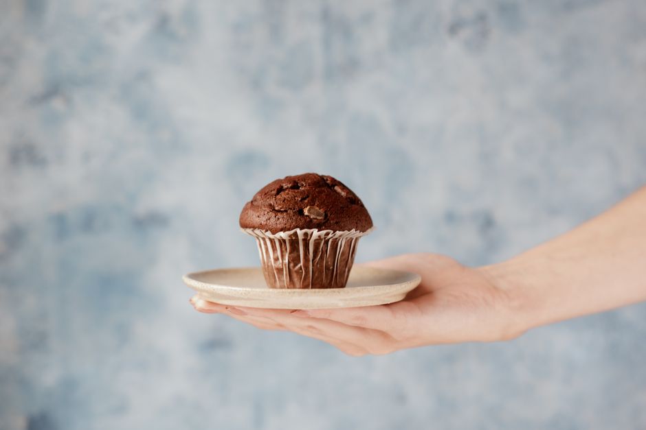 Muffins dourados de banana sobre uma grade, ao lado de bananas maduras, pote de whey e colher de mel