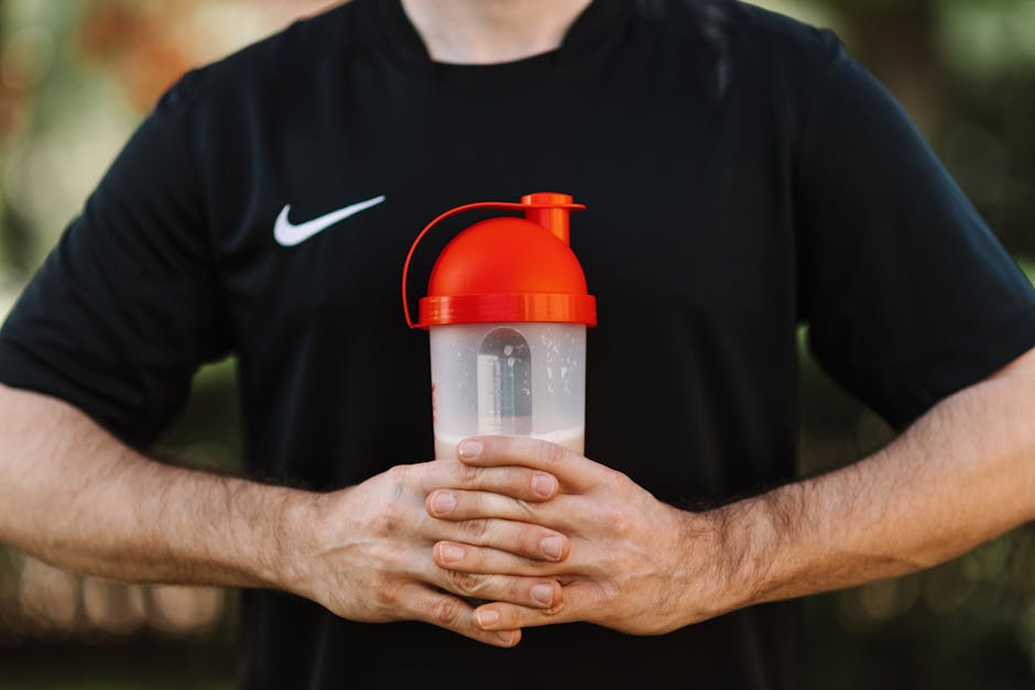 Pessoa em academia segurando um shaker moderno ao lado de um pote de whey protein isolado e frutas frescas