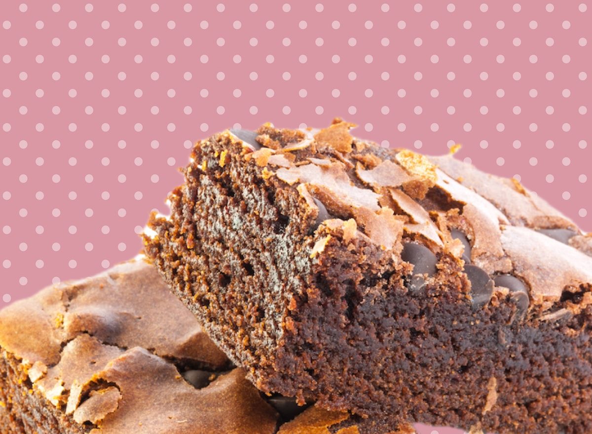 Brownie fit cortado ao meio sobre prato branco, ao lado de uma tigela de farinha de aveia, cacau em pó e mel