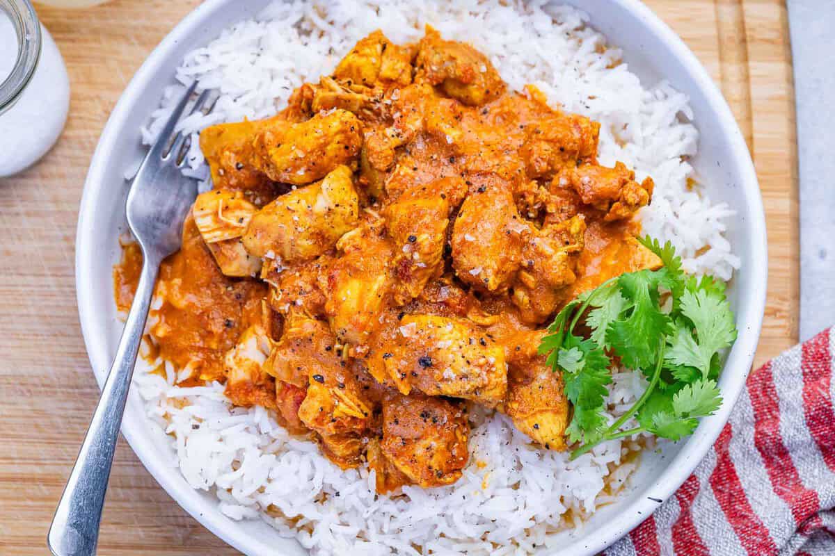 Uma tigela de arroz integral com frango grelhado e molho de tomate suave, cercada por vegetais crus