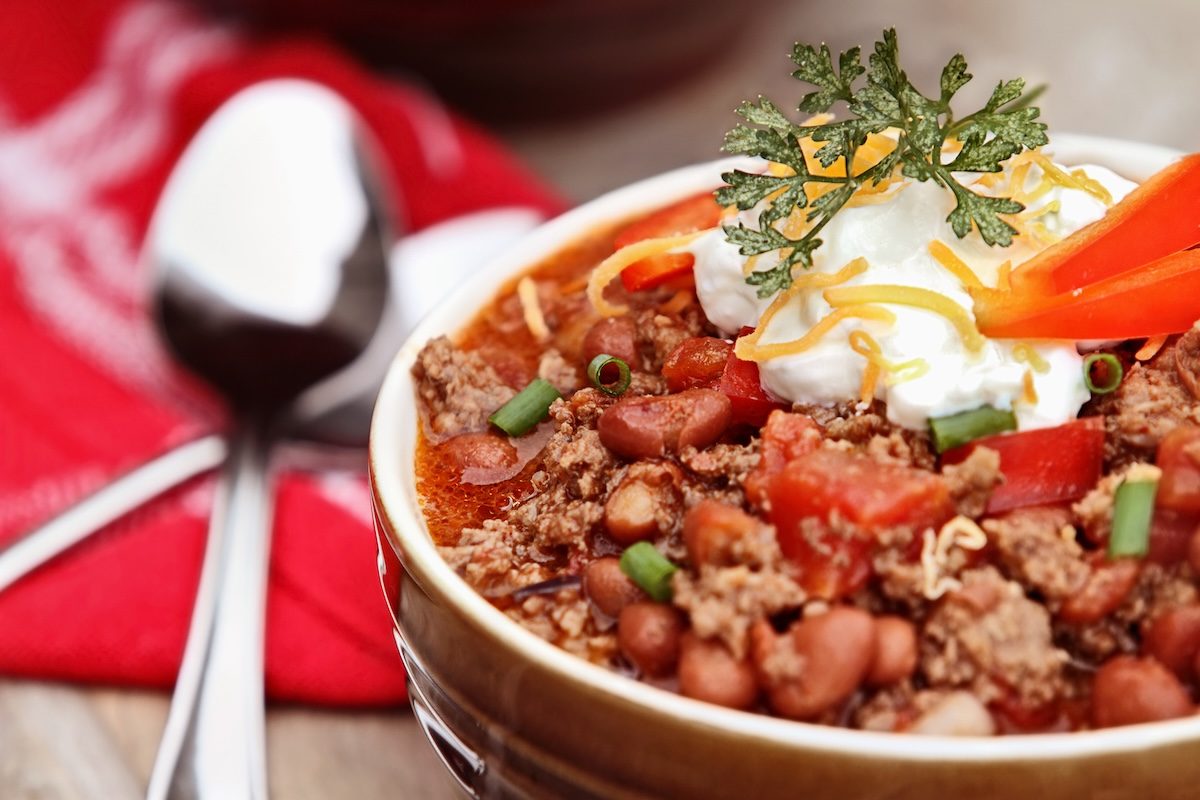 Um prato de chili quente com carne moída, feijão preto e legumes frescos, coberto por um monte de queijo derretido e pimenta