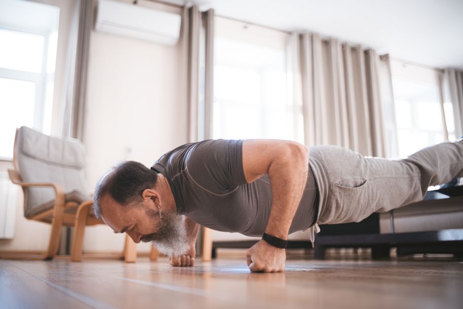 Uma senhora idosa sentada em uma cadeira, realizando um exercício de cadeira sit-to-stand com drive de joelho