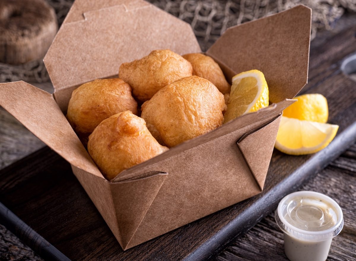 Um prato de amêijoas frescas e farinha em uma tigela ao lado de um fritadeira com bolinhos crocantes