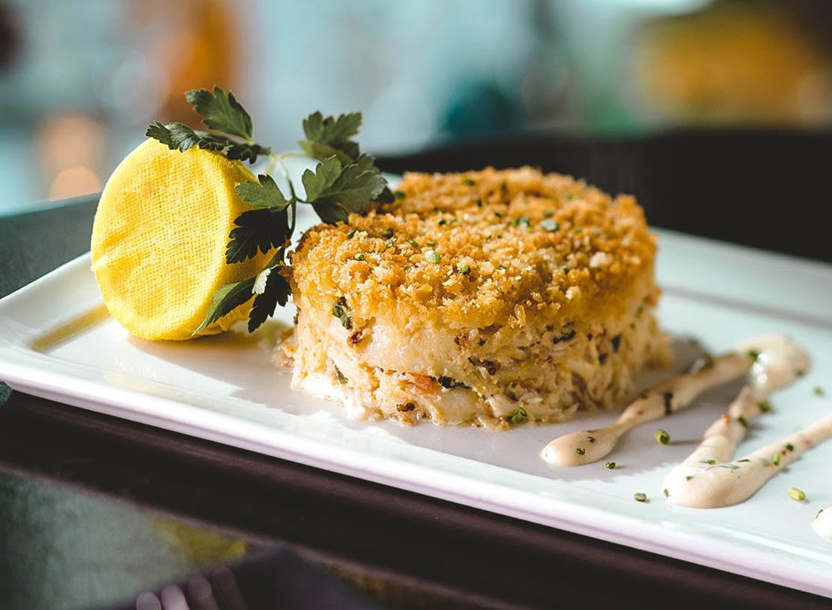 Crab cake dourado ao lado de folhas verdes, limão fatiado e quinoa, destacando proteína magra e fibras