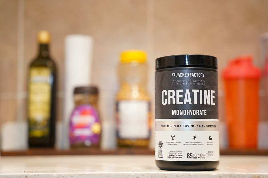 Pote de creatina monohidratada em pó com uma dose de 5g e uma garrafa de água ao lado