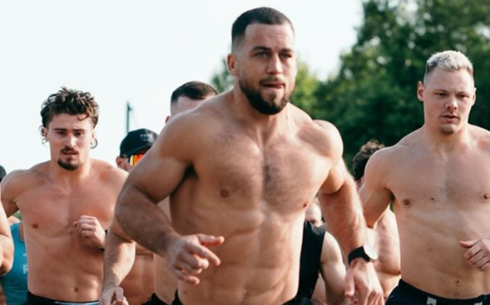 Atletas de CrossFit em ação, levantando pesos e saltando sobre caixas, com a bandeira do evento ao fundo