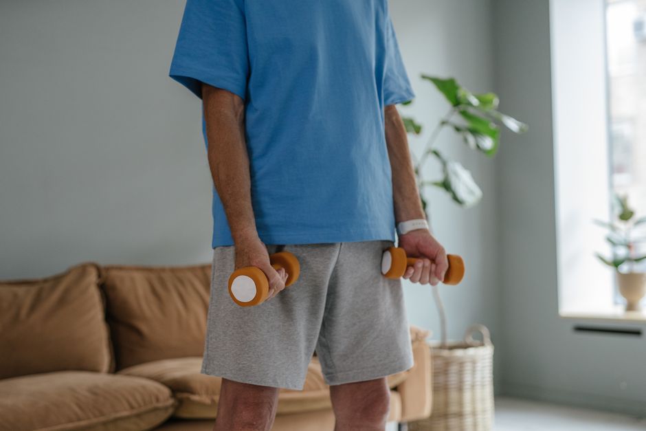 Homem de 60+ realizando agachamento goblet com kettlebell ao lado de halteres e barra para exercícios compostos