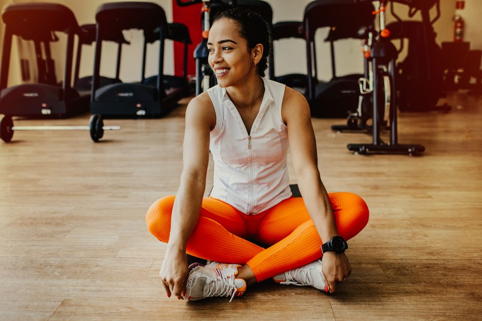 Idoso sentado numa cadeira, levantando um pé enquanto segura o encosto, ao lado de garrafa d'água e tapete