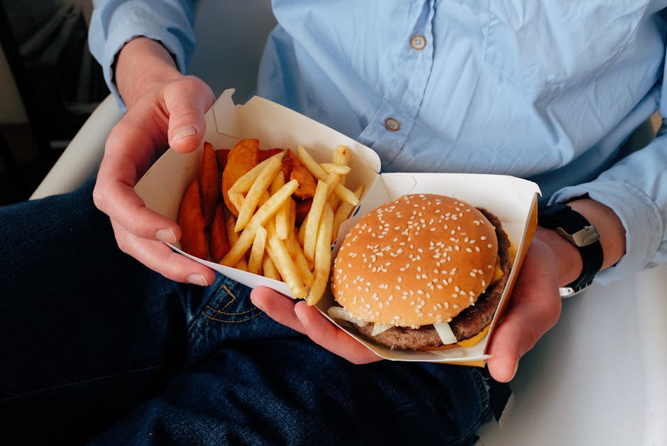 Pessoa segurando um hambúrguer em uma mão e uma salada na outra, ilustrando a escolha entre fast-food e alimentação