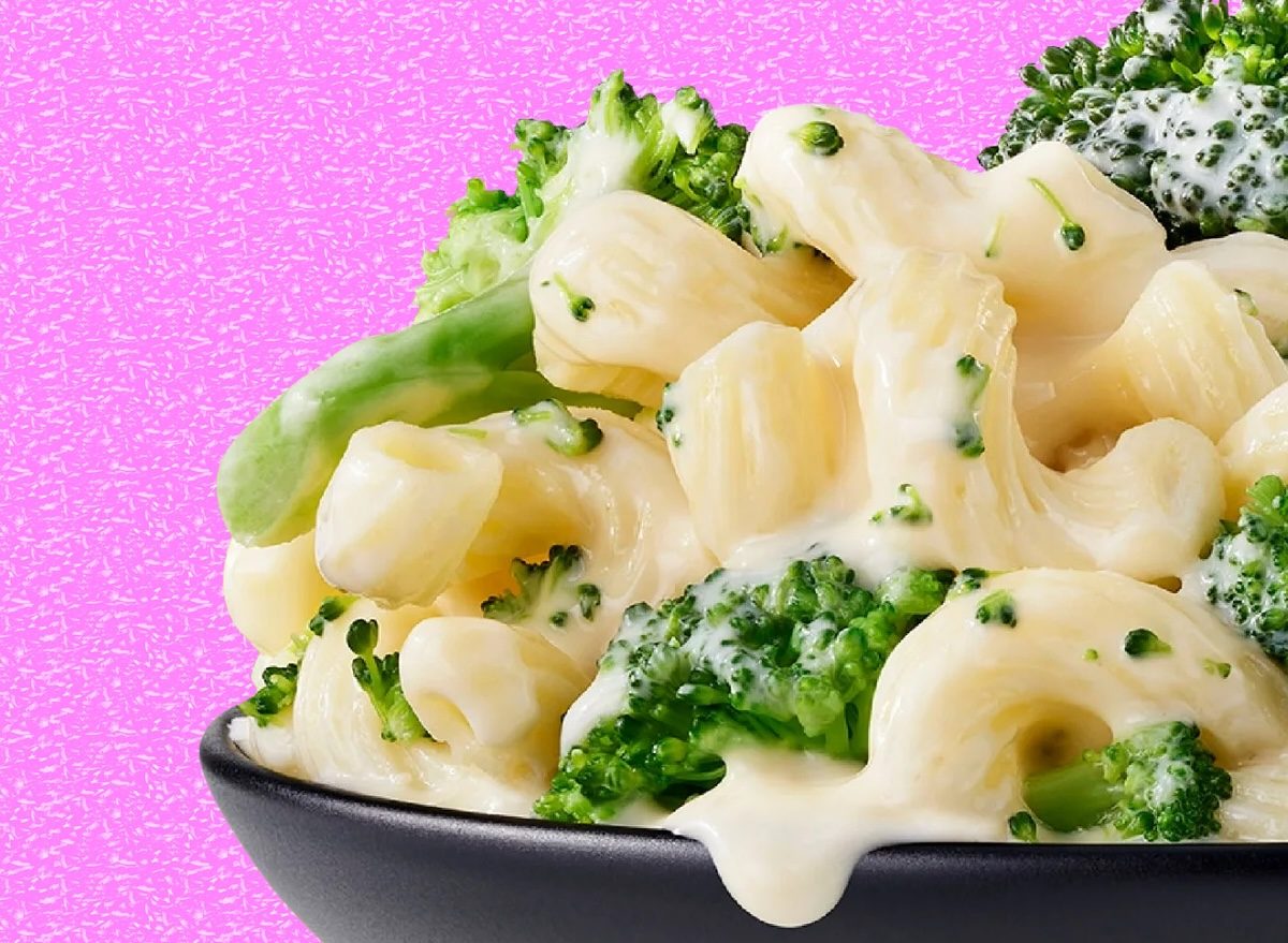 Mac and cheese congelado ao lado de um copo de whey, colher de medida e halteres, sugerindo refeição pós‑treino