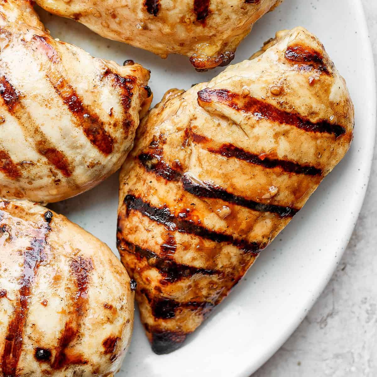 Um frango grelhado sendo preparado com uma marinada cítrica, com fatias de limão e gengibre ao redor