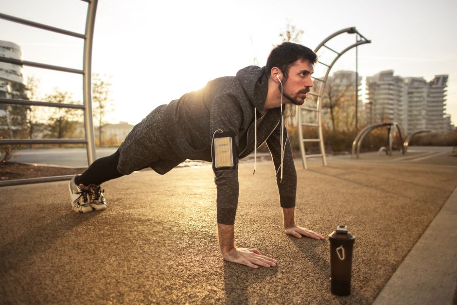 Um homem idoso em trajes de ginástica, realizando um agachamento com peso em cada mão, em um ambiente de treinamento de força