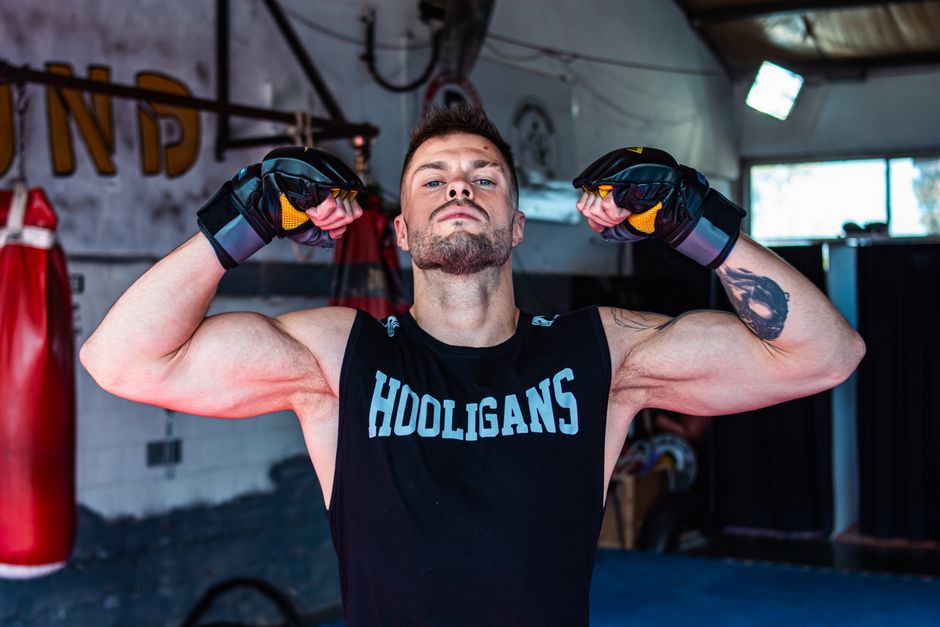 Um homem musculoso, com músculos definidos, em movimento, rodeado por frutas e legumes saudáveis e um peso de aço