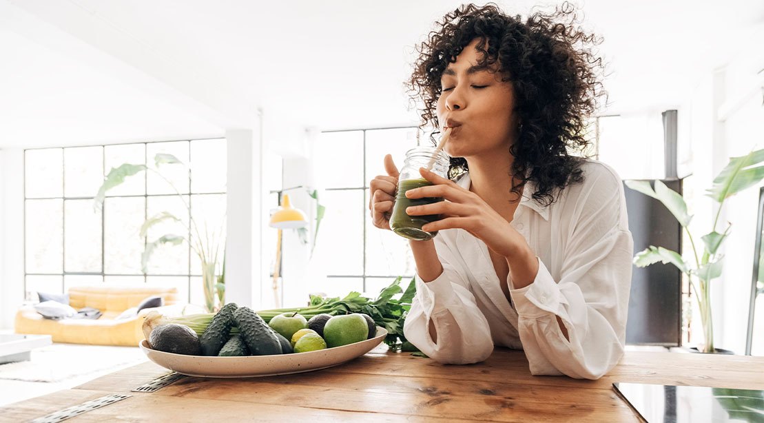 Um smoothie com frutas frescas, proteína em pó e nozes, sobre uma mesa de madeira com um liquidificador ao fundo