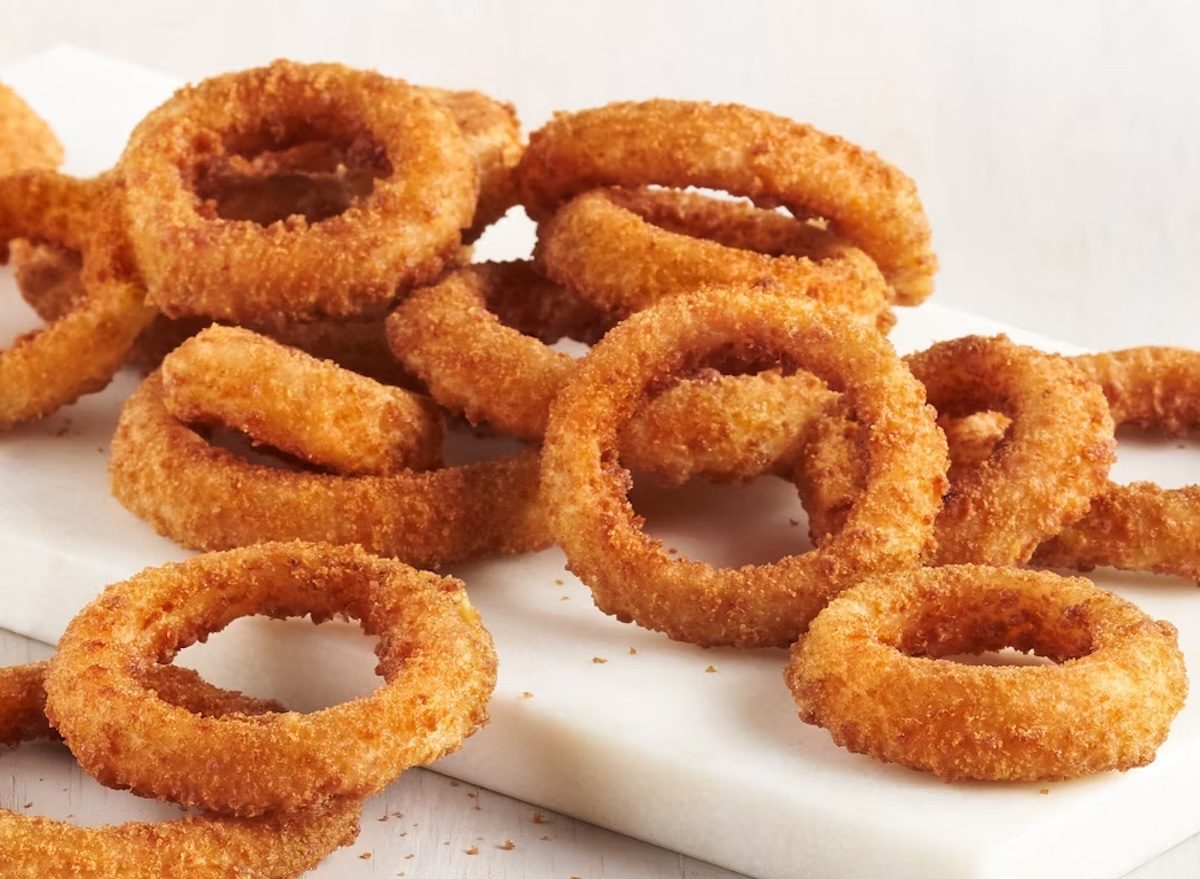 Uma mulher segurando uma bandeja de frango grelhado com onion rings congeladas crocantes