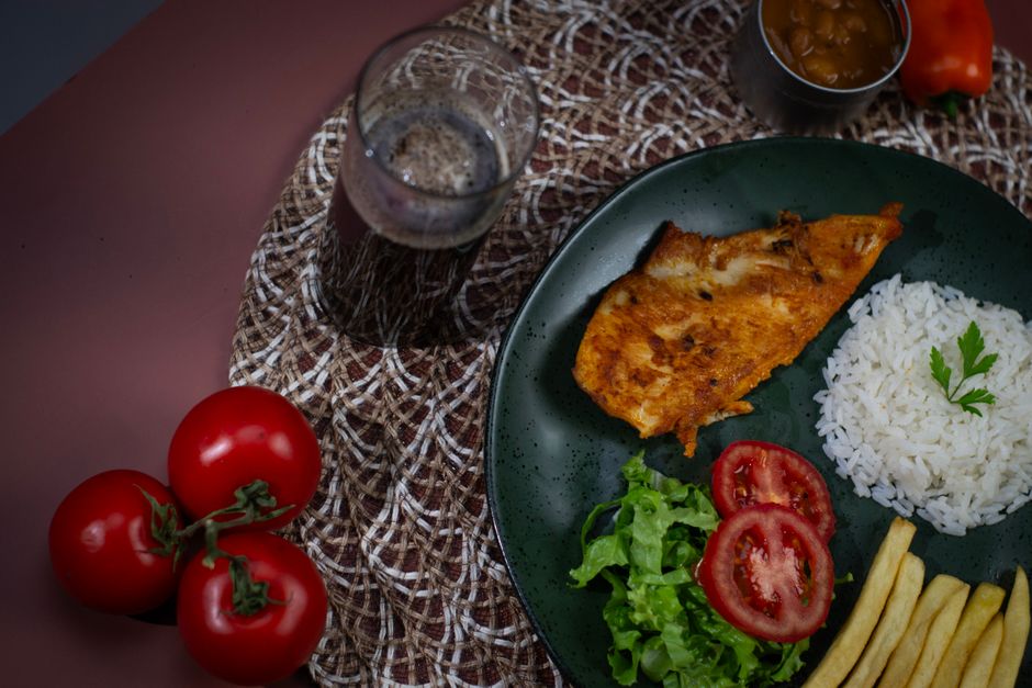 Um peixe frito dourado, servido em um prato com uma salada de repolho fresca e uma colher de azeite à mesa