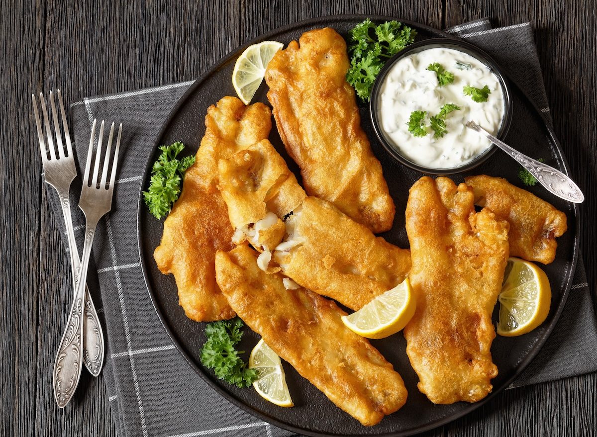 Filé de peixe frito crocante ao lado de limão, alecrim e salada de folhas verdes, servido em prato branco