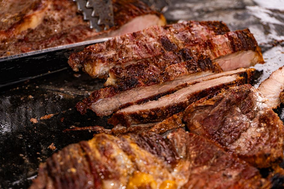 Um pork chop assado no forno, com uma crosta dourada e vetas de gordura, em uma tábua de madeira escura
