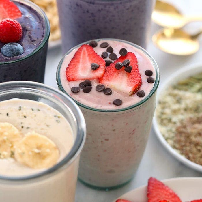 Copo de shaker ao lado de potes de whey, caseína e proteína vegetal, com frutas, amêndoas e folhas verdes