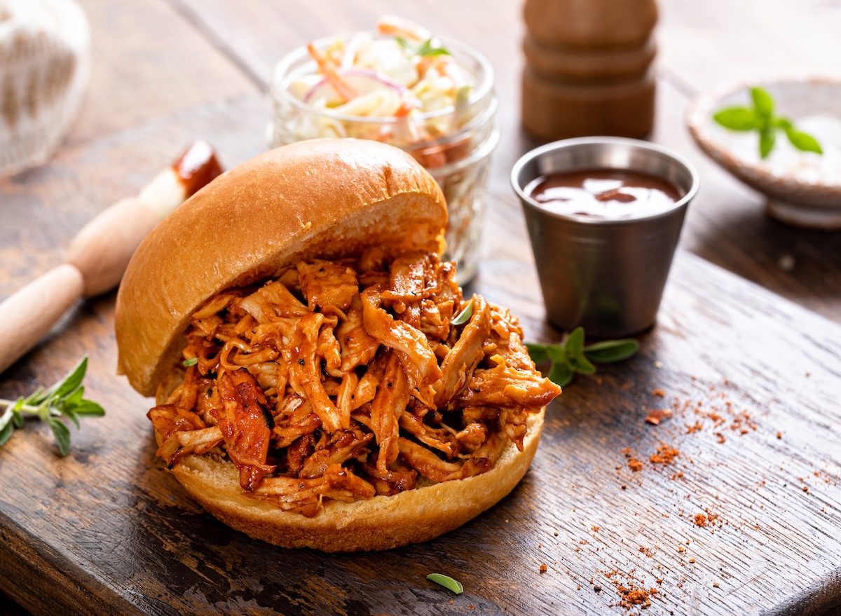 Um prato de pulled chicken com frango desfiado, temperado e servido em um prato com vegetais frescos e uma fatia de pão