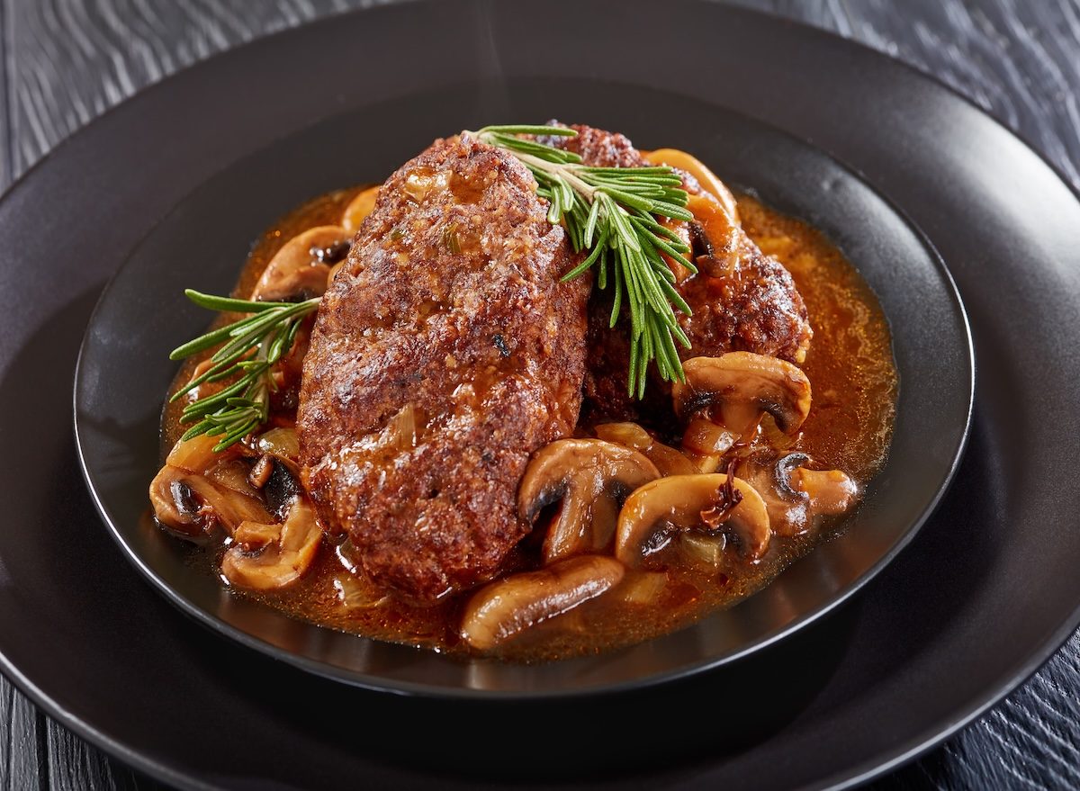 Uma mulher saudável segurando um prato de salisbury steak congelado com vegetais frescos ao lado