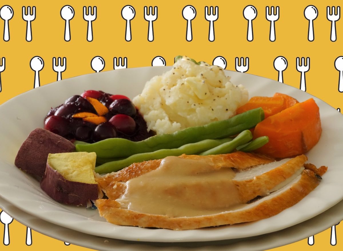 Prato com porção de peru assado congelado ao lado de purê de batata, molho de cranberry e legumes grelhados em um fundo de cozinha