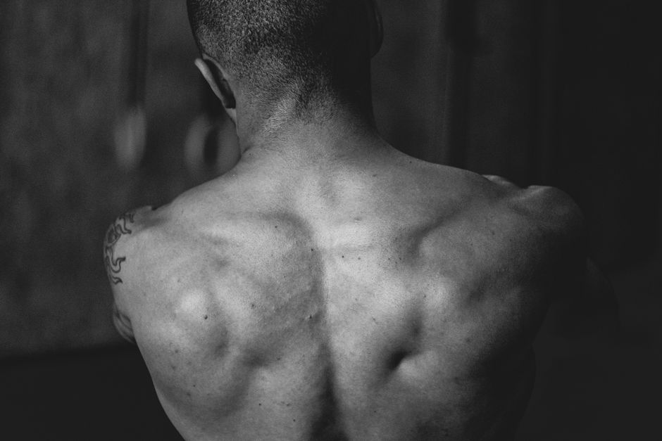 Mão segurando um haltere leve, corpo em posição de flexão contra a parede, com cotoveleiro dobrado e ombro alinhado, enquanto exibe uma garrafa de água ao lado